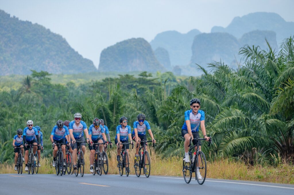 Groupe de cyclistes sur une route bordée de végétation tropicale, avec des collines calcaires au fond