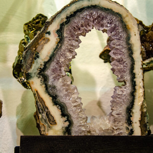 Amethyst geode with an open arch of pale crystals on a dark wooden base, soft light falling across it