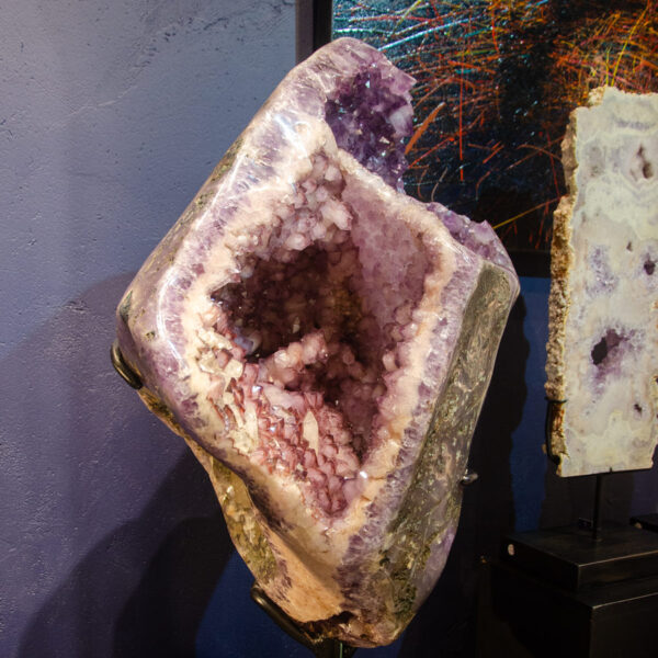 Amethyst geode on a stand with a dark wooden base, lit from the front in the Fe2 Crystals gallery