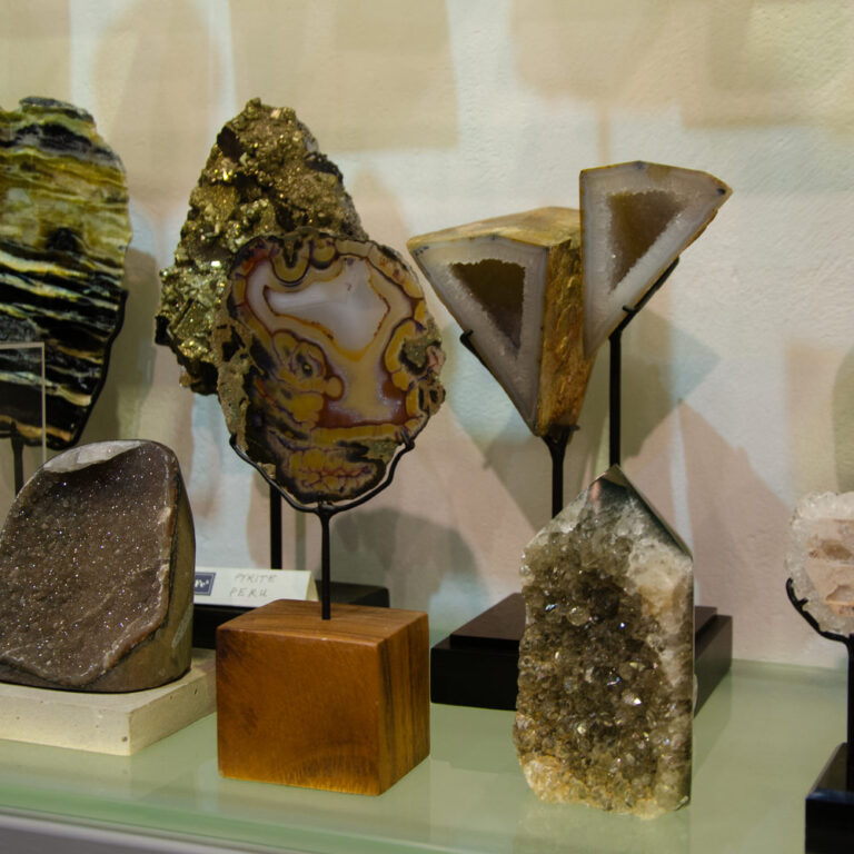 Crystals and agate slices on a glass shelf, mounted on black metal stands, a wooden block and a pale stone base