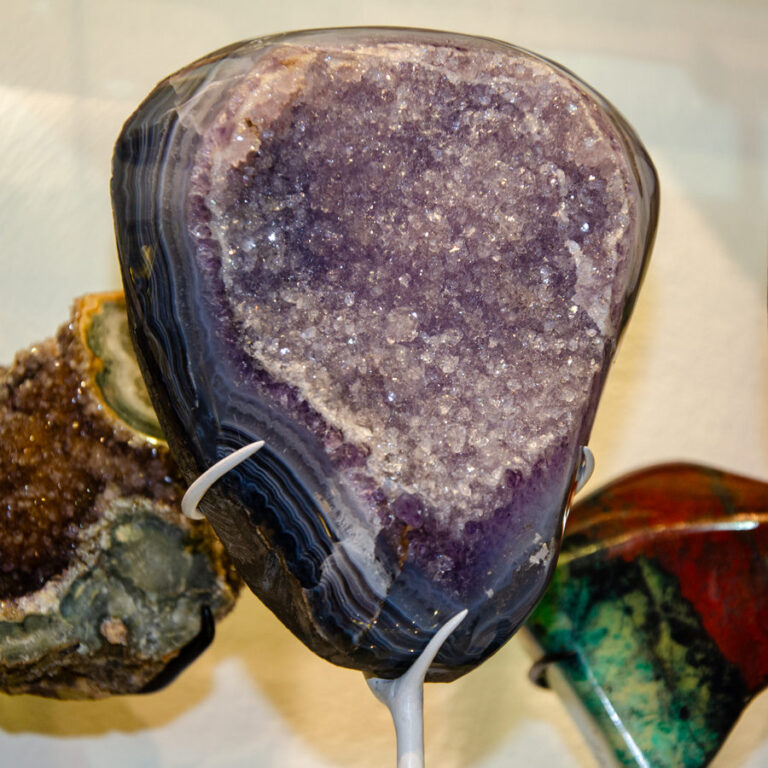 Polished amethyst geode with a banded grey rim and a glittering druzy face, on a thin white stand
