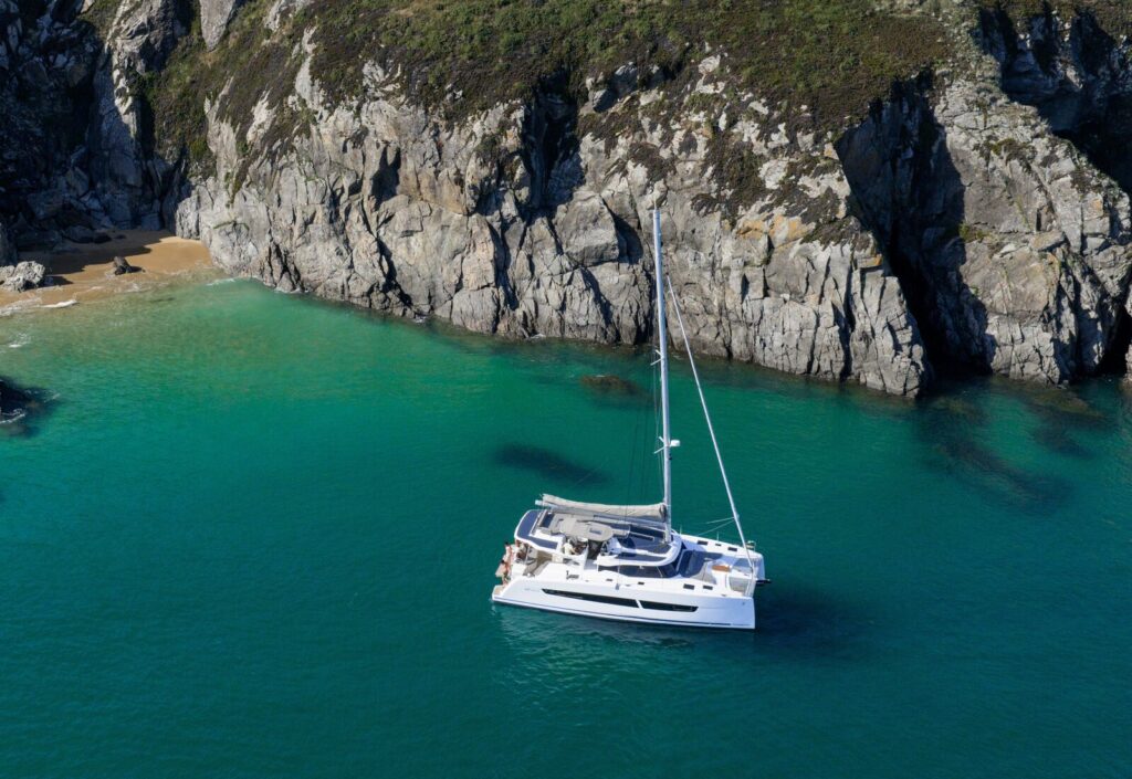 Catamaran at anchor in a bay below rocky cliffs
